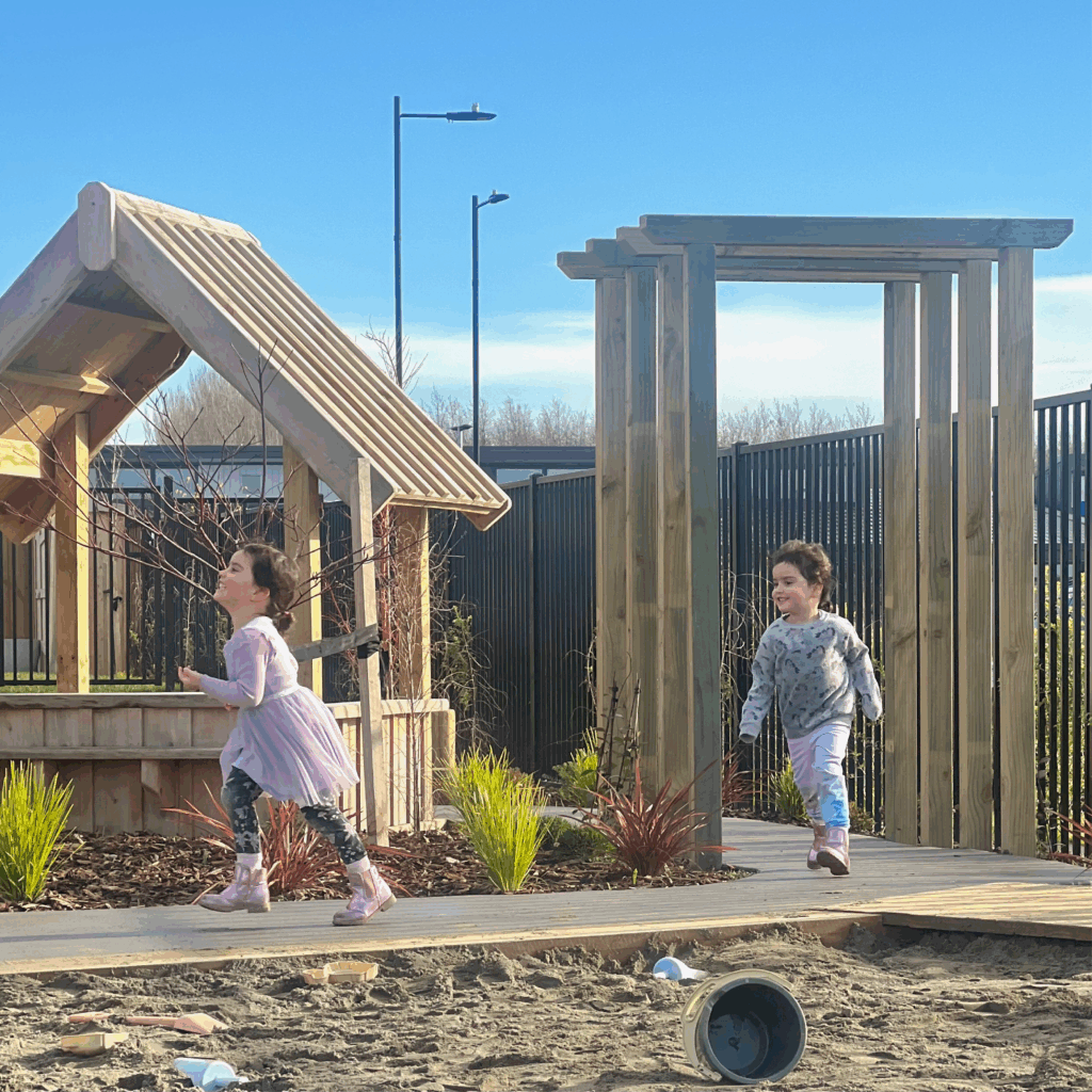 Girls running past a cubby house and sandpit